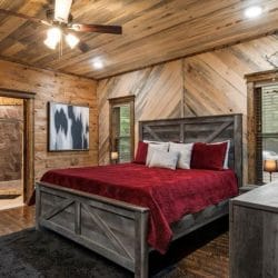 King bed with a red bedspread and gray headboard, bathroom doorway beside it