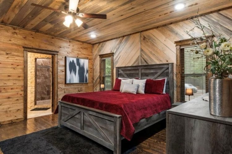 King bed with a red bedspread and gray headboard, bathroom doorway beside it