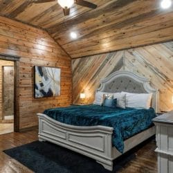 King bed with teal bedding and a white upholstered headboard on a diagonal-plank wall