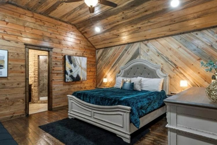King bed with teal bedding and a white upholstered headboard on a diagonal-plank wall