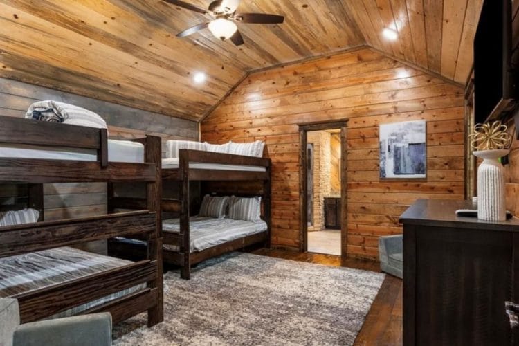 Bunk room with two sets of stacked queen beds, a TV and a doorway to a bathroom