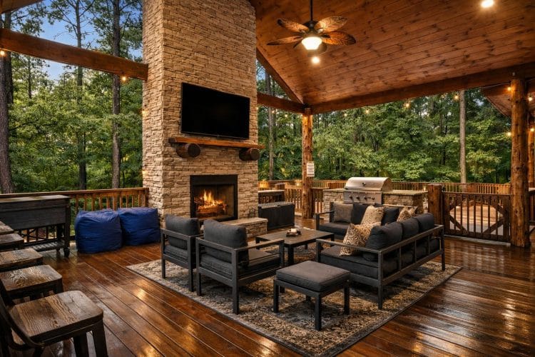 Covered deck with a stone fireplace, wall-mounted TV and an outdoor seating group