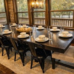 Long dark dining table set with plates and black chairs in front of a wall of windows