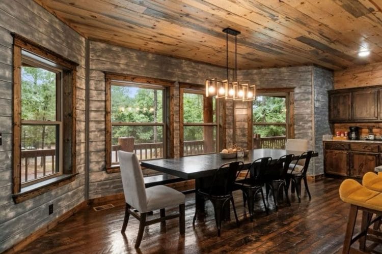 Dining table beside tall windows and a stone wall under pendant lights