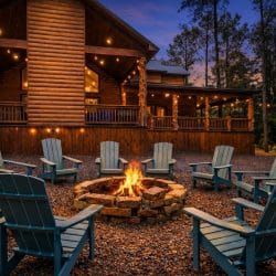 Fire pit surrounded by Adirondack chairs at dusk with the lodge lit up behind it