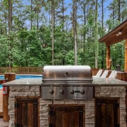Stainless built-in grill in a stone counter with the pool deck behind it