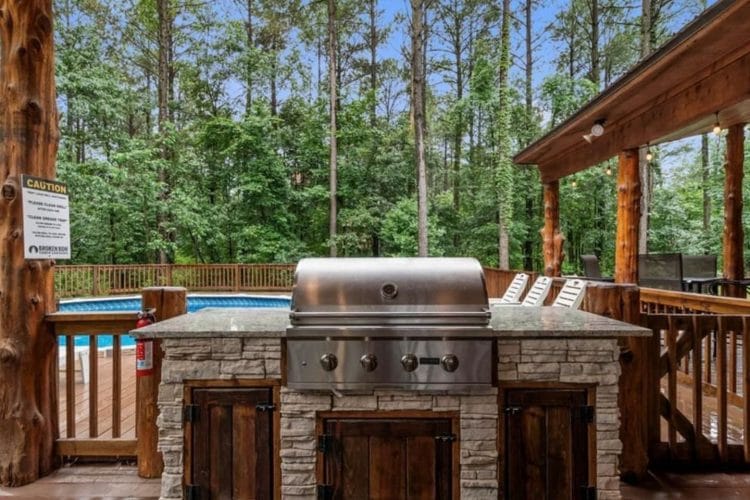 Stainless built-in grill in a stone counter with the pool deck behind it