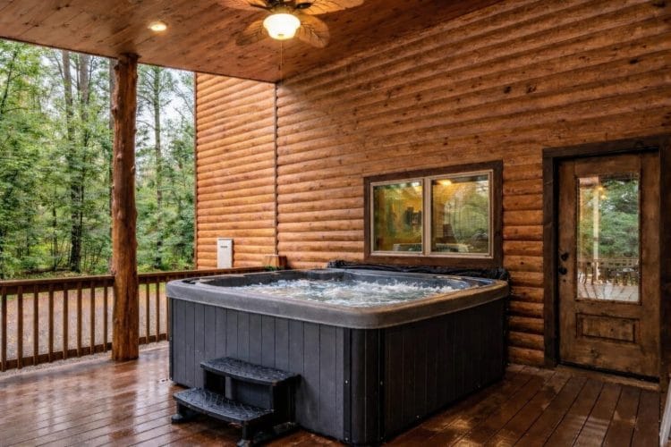Hot tub on the covered porch beside a log wall and a door