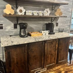 Coffee bar with a granite top, drip coffee maker and mugs on a shelf above