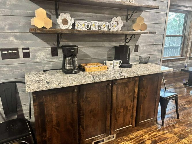 Coffee bar with a granite top, drip coffee maker and mugs on a shelf above
