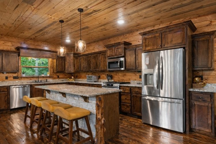 Kitchen with a granite-topped island and bar stools, stainless fridge and wood cabinets