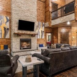 Living room with dark leather sofas and a stone fireplace with a TV above it, loft railing overhead