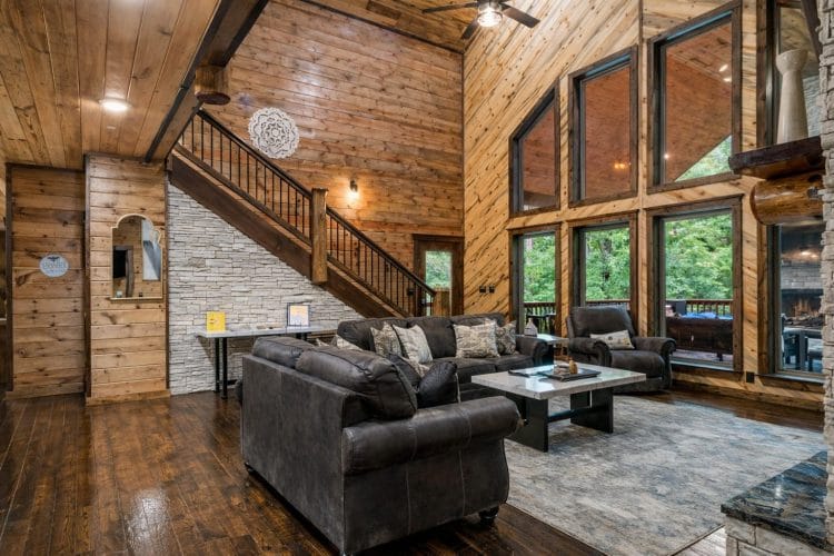 Living room seating with the wood staircase and tall windows behind