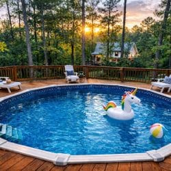 Round above-ground pool inside a wood sun deck with loungers, pine trees behind