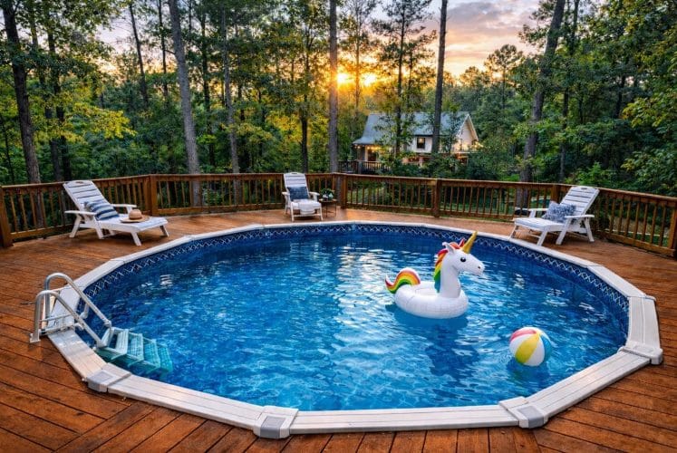 Round above-ground pool inside a wood sun deck with loungers, pine trees behind