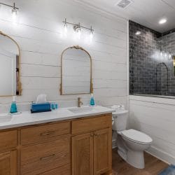 Double vanity with two arched gold mirrors and a glass walk-in shower with dark tile
