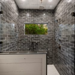 Large walk-in shower with dark brick-style tile and a window