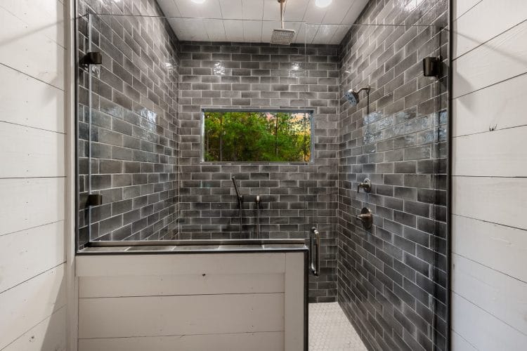 Large walk-in shower with dark brick-style tile and a window