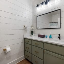 Bathroom vanity with sage-green cabinets, a black faucet and a black-framed mirror