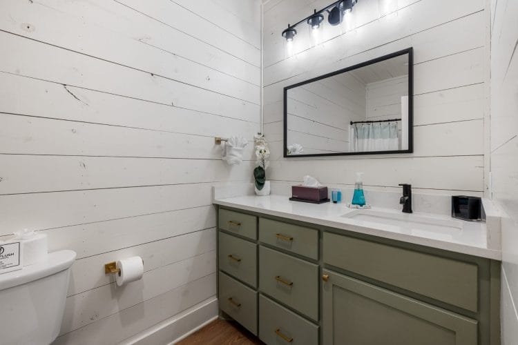 Bathroom vanity with sage-green cabinets, a black faucet and a black-framed mirror