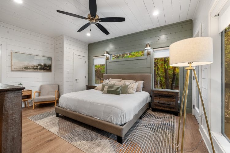 Same bedroom with a tripod floor lamp and a window beside the bed