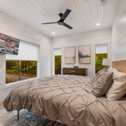 Upstairs bedroom with a wood-slat headboard, gray pintuck bedding, a ceiling fan and a wall-mounted TV