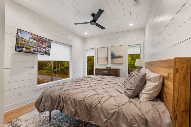 Upstairs bedroom with a wood-slat headboard, gray pintuck bedding, a ceiling fan and a wall-mounted TV