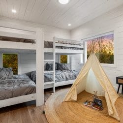 Bunk room with a white twin-over-twin bunk, a canvas teepee on a jute rug and a bedside table