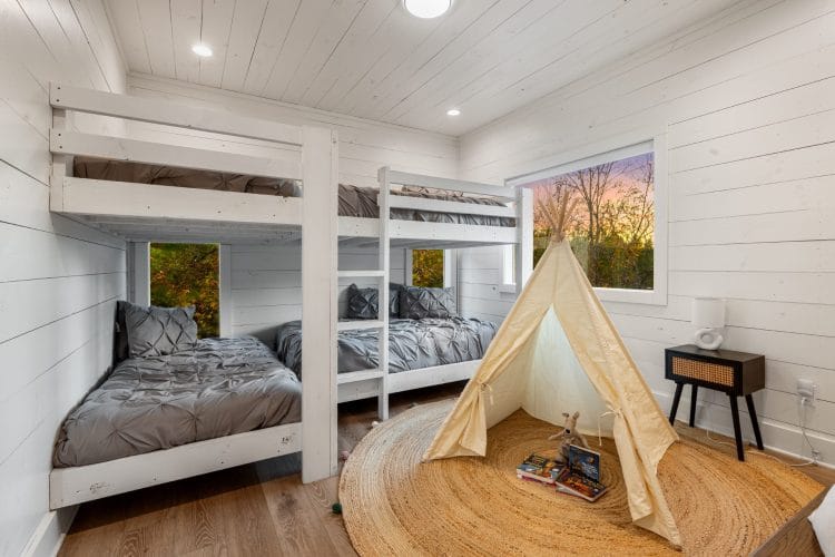 Bunk room with a white twin-over-twin bunk, a canvas teepee on a jute rug and a bedside table