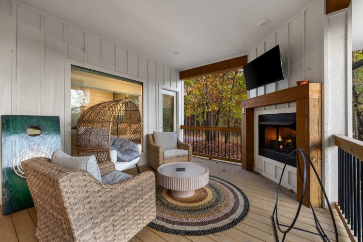 Covered patio with wicker chairs, a gas fireplace with a TV above it and a wicker egg chair