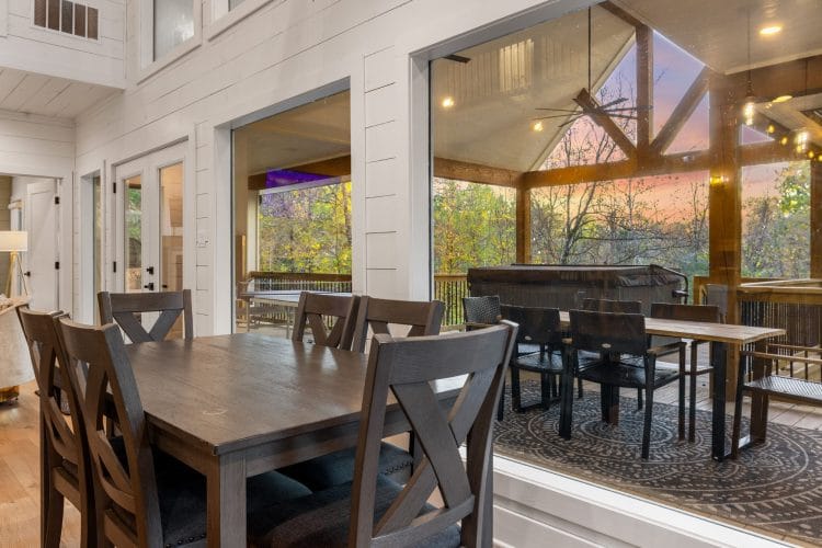 Wood dining table with X-back chairs beside a window onto the covered deck