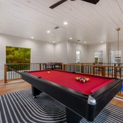 Pool table on a black-and-white rug in the loft, with a railing that overlooks the main room