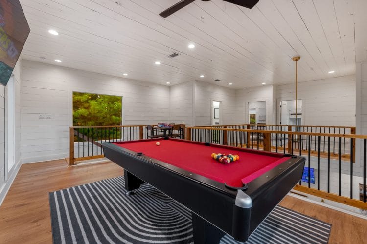 Pool table on a black-and-white rug in the loft, with a railing that overlooks the main room