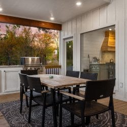 Outdoor dining table with black chairs beside a counter and grill on the covered deck