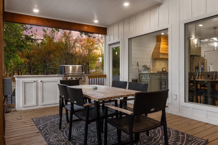 Outdoor dining table with black chairs beside a counter and grill on the covered deck