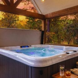 Hot tub under a covered deck roof, with bathrobes, slippers and drinks on a side table