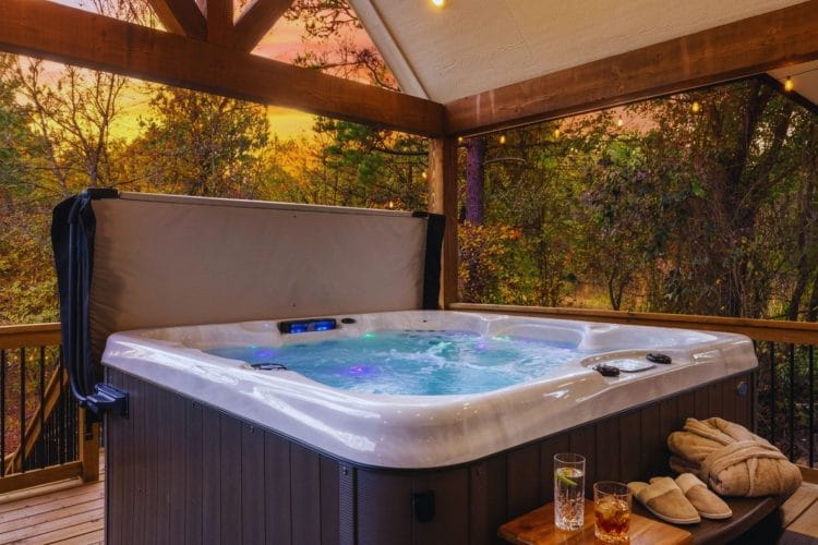 Hot tub under a covered deck roof, with bathrobes, slippers and drinks on a side table