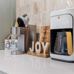 Countertop coffee maker beside a wooden JOY sign