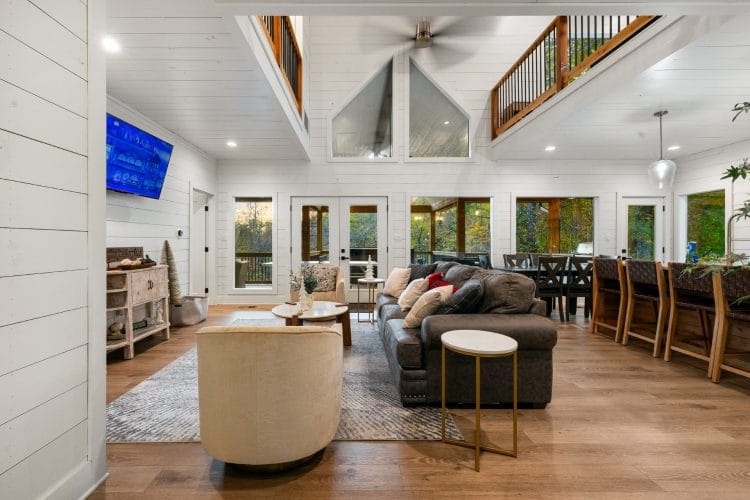 Open main room with a tan armchair and sofas, and bar stools along the kitchen counter