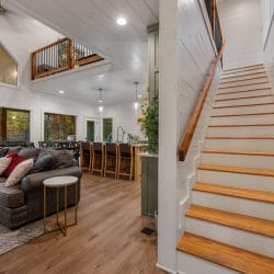 Wooden stairs with a white railing climbing from the main room to the loft