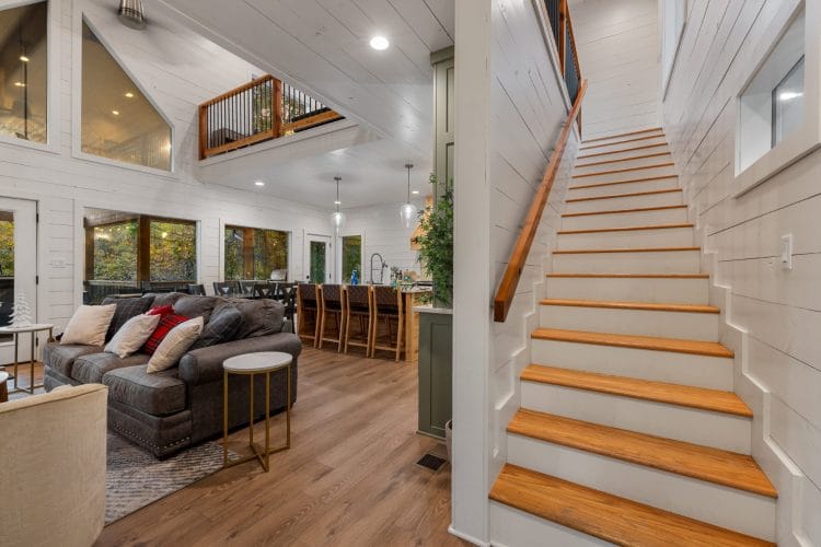 Wooden stairs with a white railing climbing from the main room to the loft