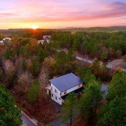 Aerial view of the white cabin among pines and hardwoods at sunset