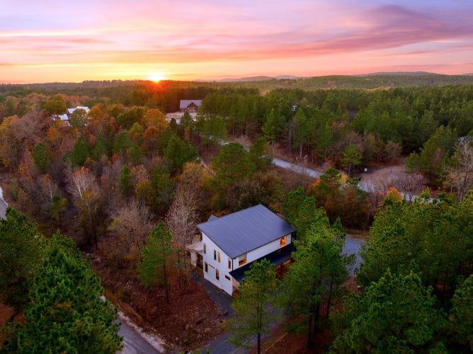 Aerial view of the white cabin among pines and hardwoods at sunset