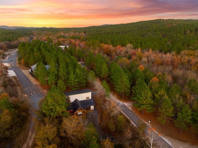 Aerial view of the cabin and gravel road through the trees at sunset