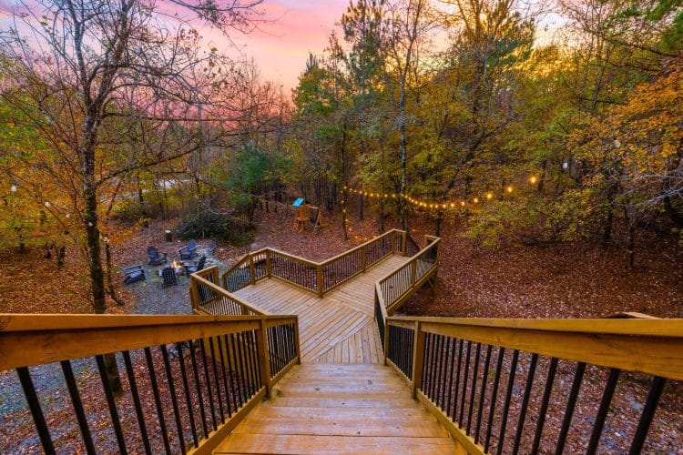 Wooden deck stairs and walkway leading down to the fire pit area, string lights above