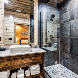 Bathroom with a vessel sink on a rustic vanity and a dark-tile walk-in shower