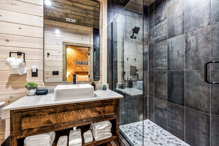 Bathroom with a vessel sink on a rustic vanity and a dark-tile walk-in shower