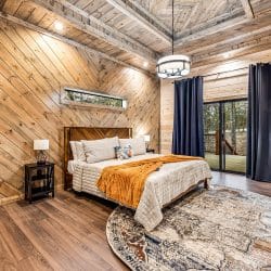 King bed with an orange throw and navy curtains beside a sliding glass door, pine walls