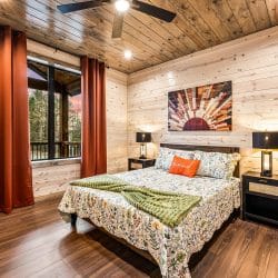 Queen bedroom with a floral comforter, orange curtains and a sunburst wall piece
