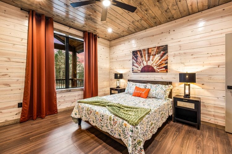 Queen bedroom with a floral comforter, orange curtains and a sunburst wall piece